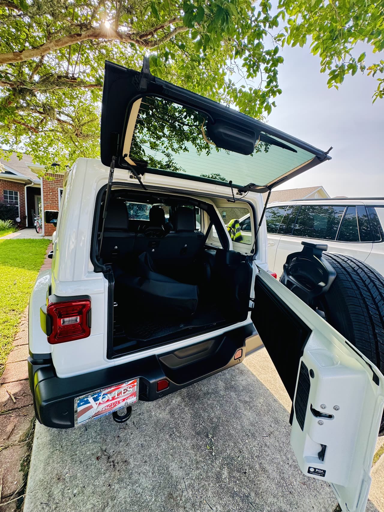 White 2025 Jeep Wrangler Sahara with the rear liftgate open, showing cargo space and the full-size spare tire
